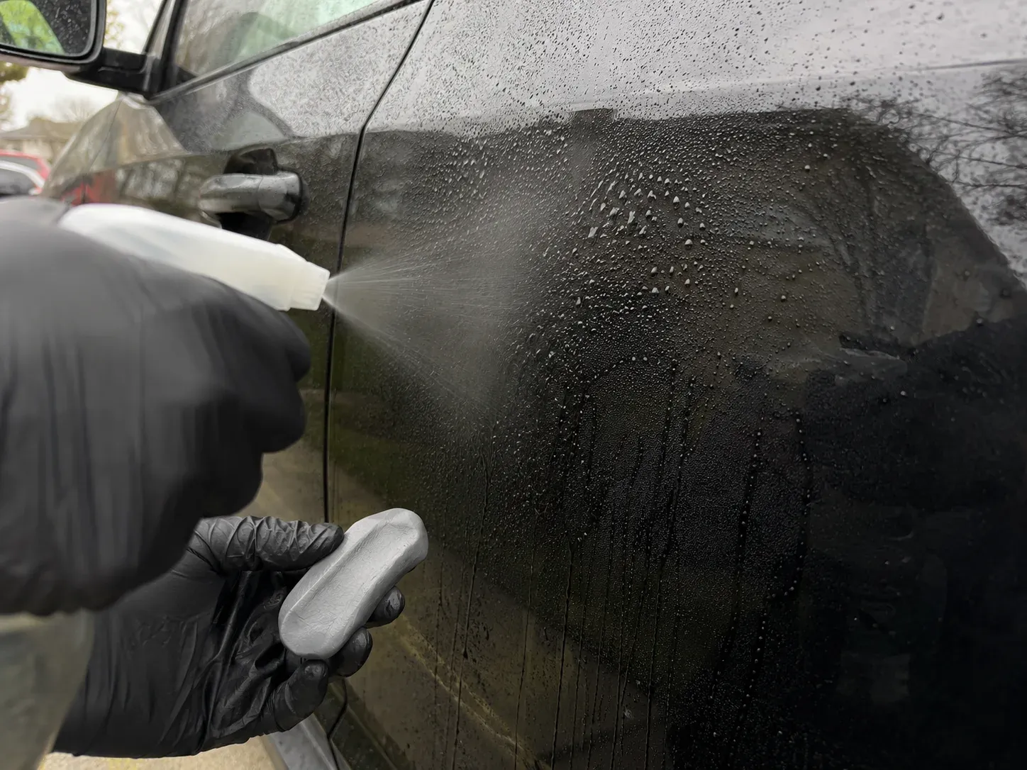 Spraying lubricant before clay bar treatment step on black car door